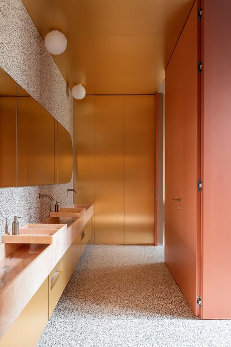 The image depicts a modern and minimalist bathroom design featuring warm, earthy tones, terrazzo flooring, and statement lighting.