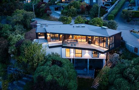 A modern, beautifully designed house nestled among lush greenery, featuring striking architectural elements and illuminated interiors.