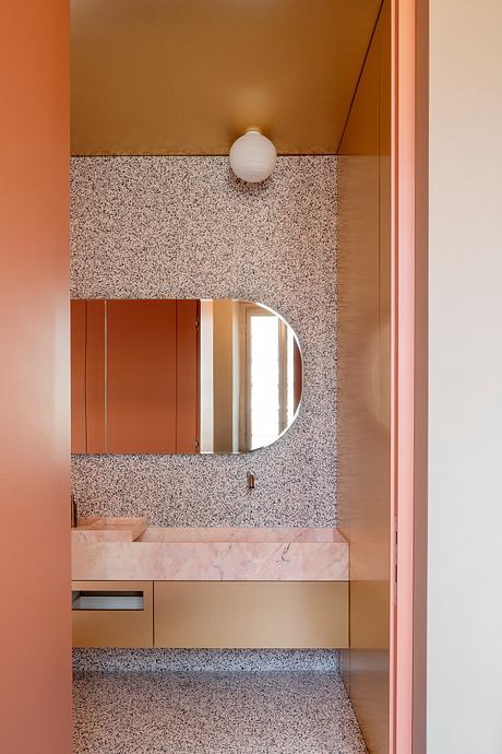 A modern bathroom with a terrazzo vanity, round mirror, and warm-toned accent walls.