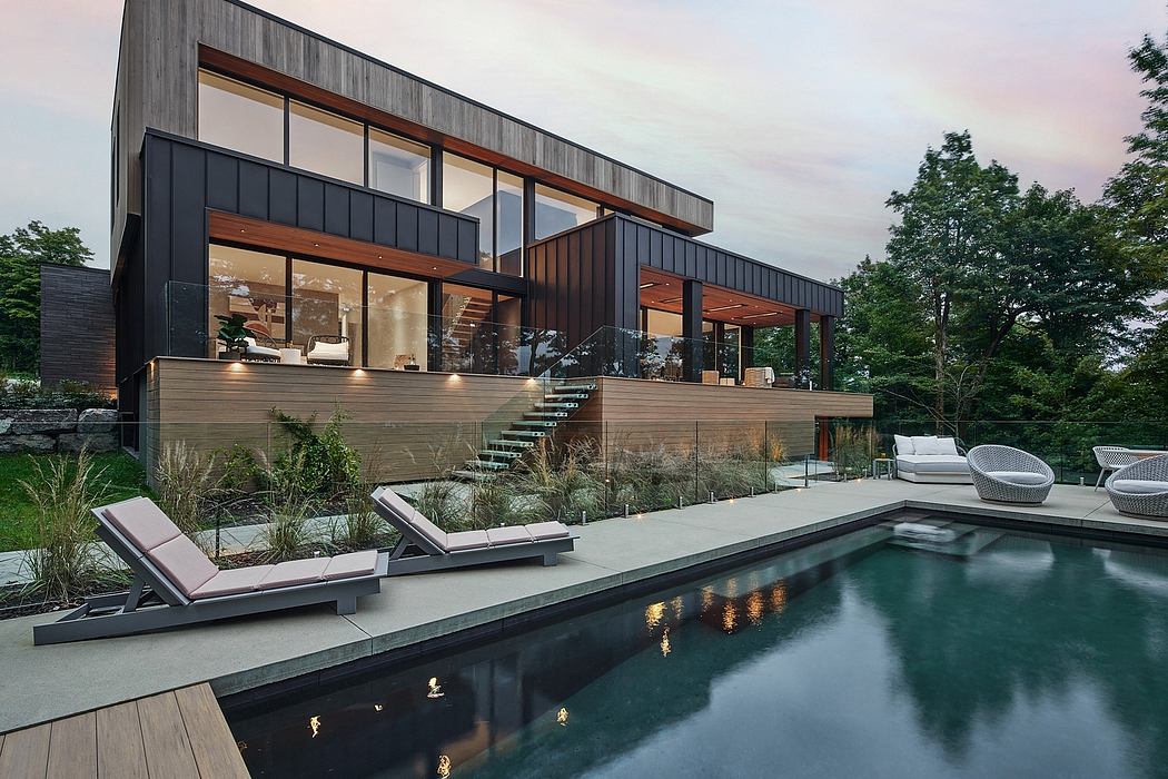 A modern, sleek house with a pool surrounded by lush greenery and a wooden deck.