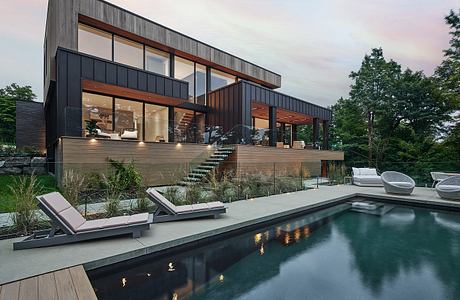 A modern, sleek house with a pool surrounded by lush greenery and a wooden deck.