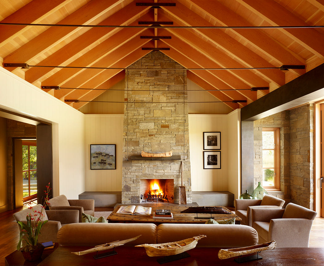 Warm, rustic interior with stone fireplace, wood-paneled ceiling, and plush seating.