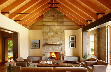 Warm, rustic interior with stone fireplace, wood-paneled ceiling, and plush seating.