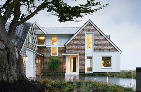 A modern, two-story home with a wooden exterior, large windows, and a wraparound porch.