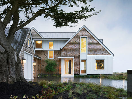 A modern, two-story home with a wooden exterior, large windows, and a wraparound porch.