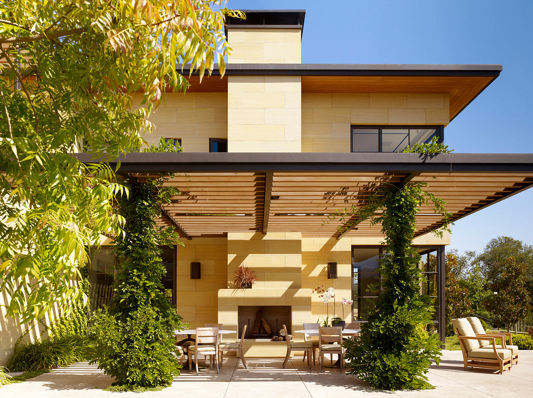 A modern home with a covered patio, wooden beams, and lush greenery surrounding the outdoor seating area.