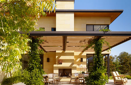 A modern home with a covered patio, wooden beams, and lush greenery surrounding the outdoor seating area.