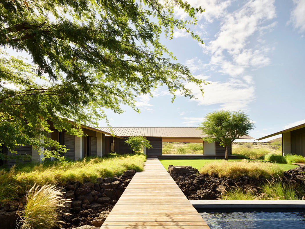 A modern single-story dwelling with a wooden walkway leading to a pool, surrounded by lush greenery.