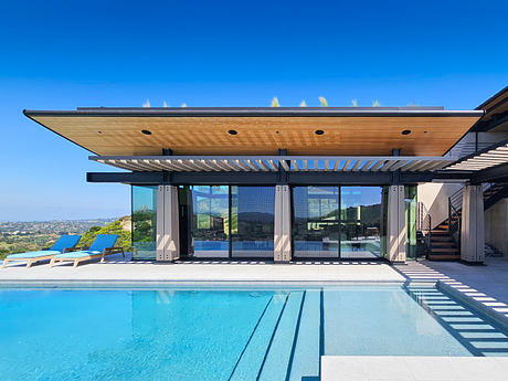 Sleek, modern architecture with wood beams, glass walls, and outdoor pool overlooking hills.