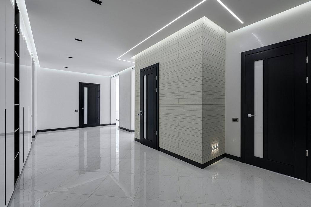 A modern, minimalist hallway with sleek black doors, white walls, and recessed lighting.