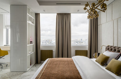 Expansive bedroom with floor-to-ceiling windows, brass chandelier, and modern furniture.