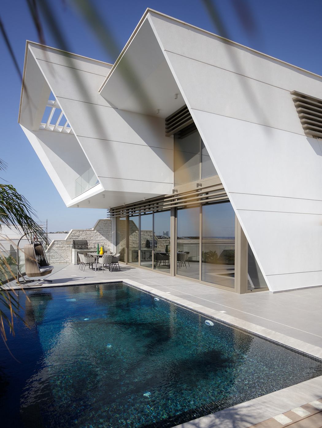Modern geometric architecture with sleek glass walls, pool, and outdoor seating area.