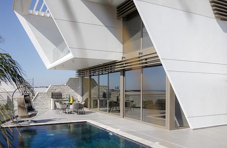 Modern geometric architecture with sleek glass walls, pool, and outdoor seating area.