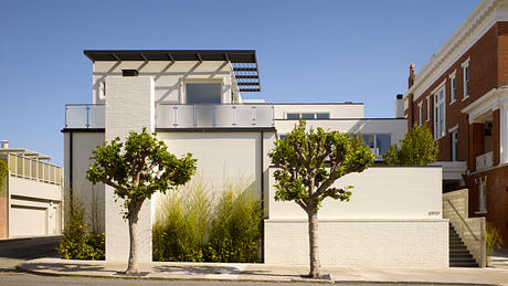 Modern white building with sleek balconies, trees, and brick accents on a sunny day.