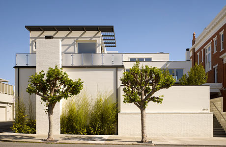 Modern white building with sleek balconies, trees, and brick accents on a sunny day.