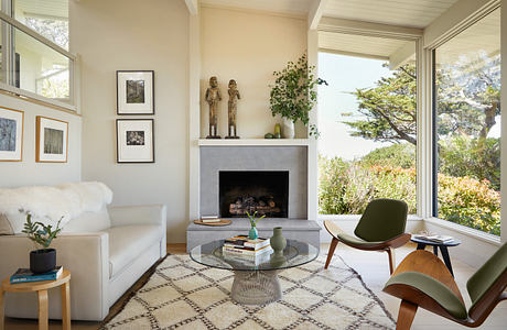 Bright, airy living room with minimalist decor, fireplace, and panoramic windows overlooking nature.