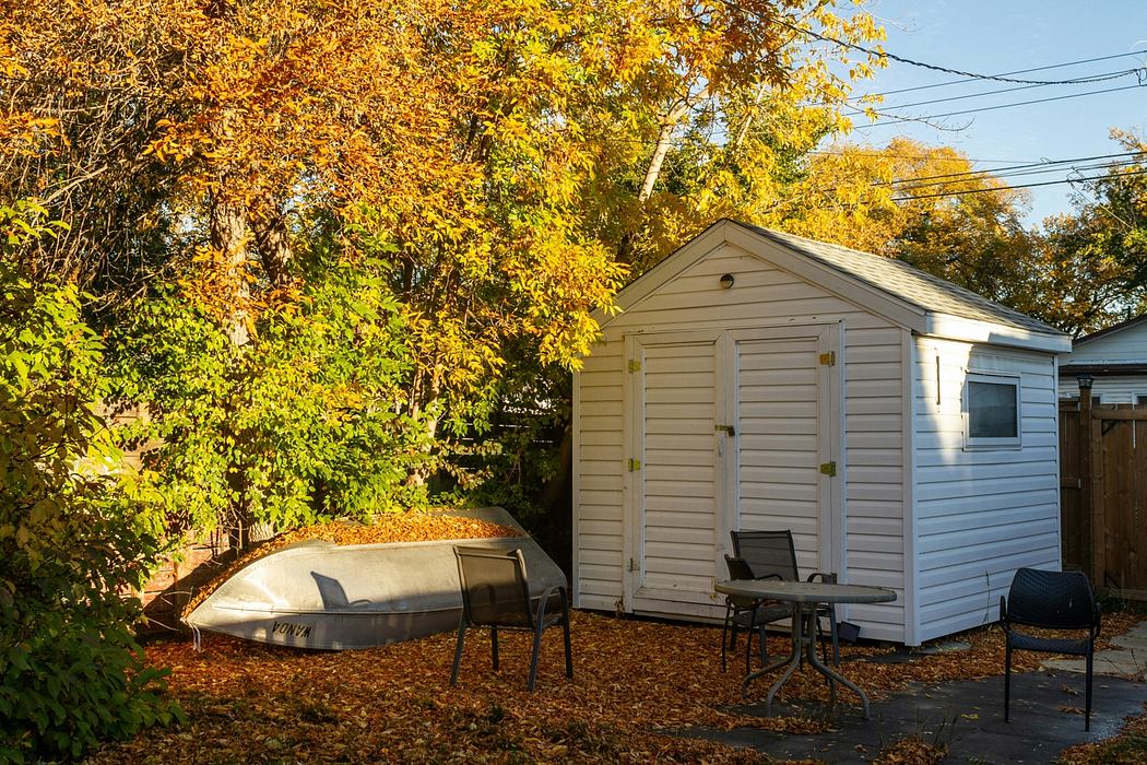 A cozy backyard shed with a boat and outdoor furniture on a carpet of fall foliage.