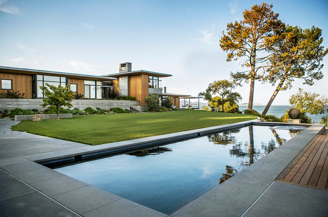 Striking contemporary home with wood and glass facade, pool reflecting surroundings.