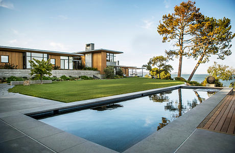 Striking contemporary home with wood and glass facade, pool reflecting surroundings.