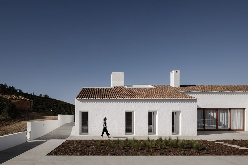 A modern, minimalistic white building with a tiled roof and large windows surrounded by landscaping.