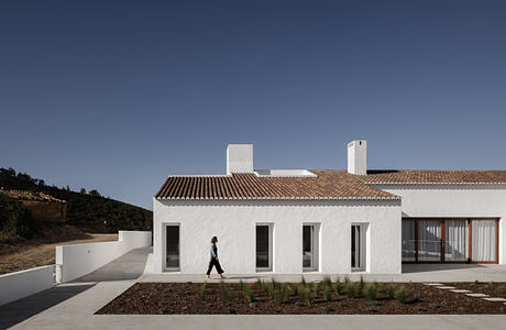 A modern, minimalistic white building with a tiled roof and large windows surrounded by landscaping.