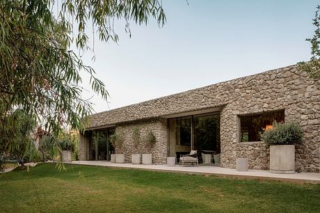 A single-story stone building with floor-to-ceiling windows, a lawn, and shrubs.