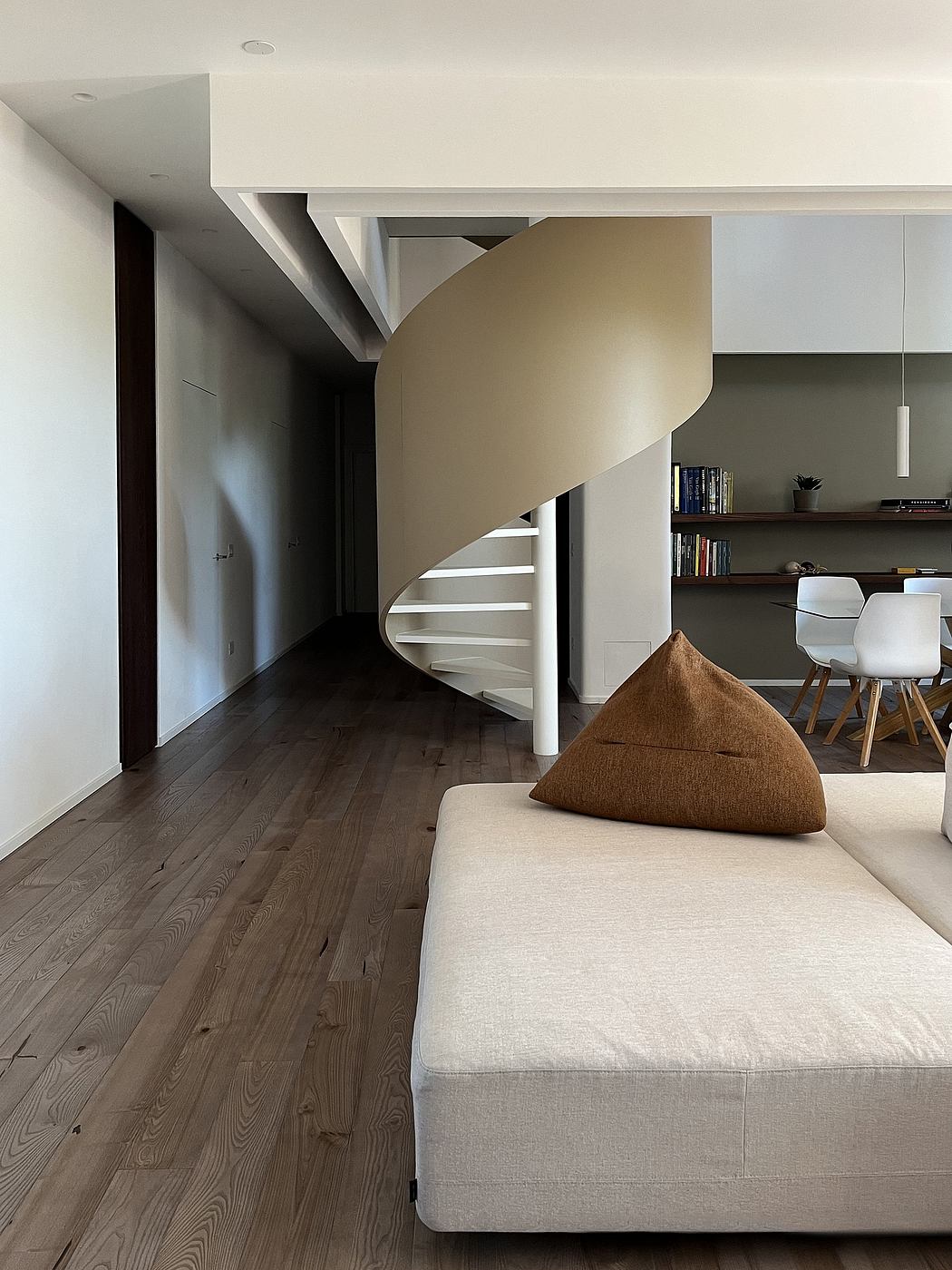 A modern, open-concept living space with a spiral staircase, built-in shelving, and minimal decor.