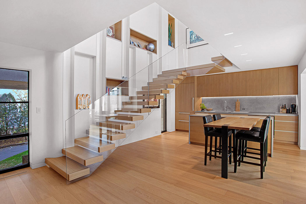Minimalist staircase design with glass panels, open plan kitchen-dining area, hardwood flooring.