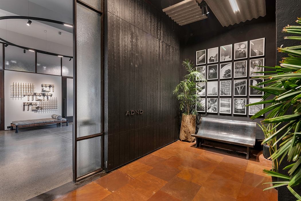 Entrance lobby with dark wooden panels, framed art displays, and a metal bench against a lush plant.