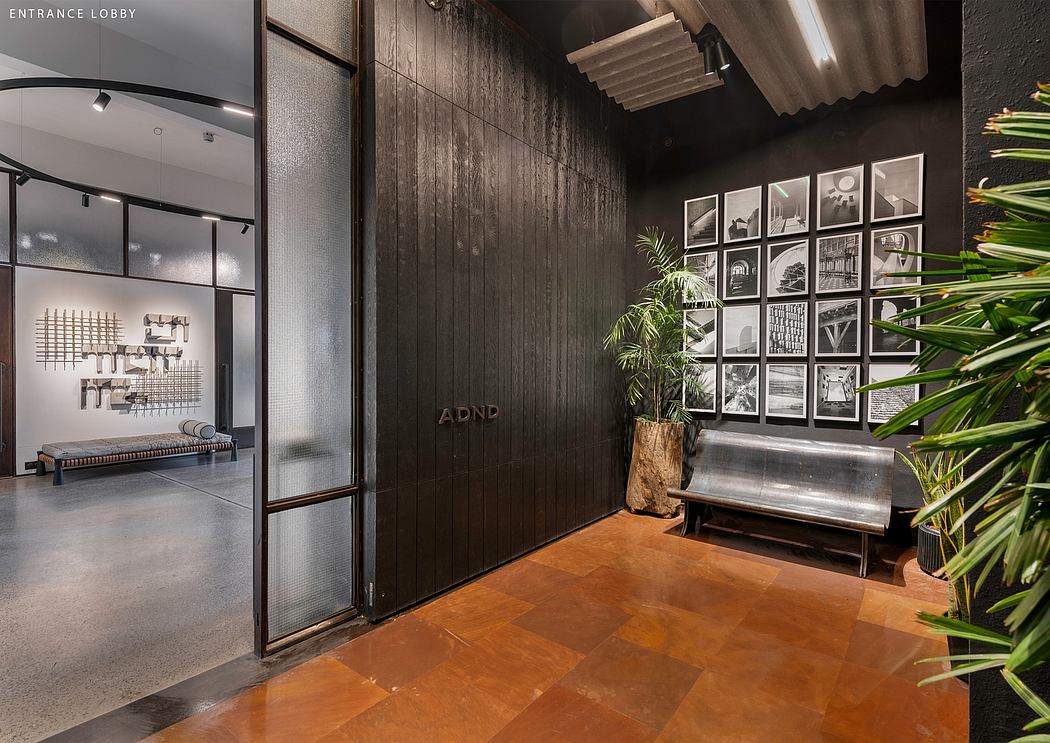 Entrance lobby with dark wooden panels, framed art displays, and a metal bench against a lush plant.