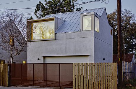 A modern, two-story residence with a striking angular roof, large windows, and a wooden fence.