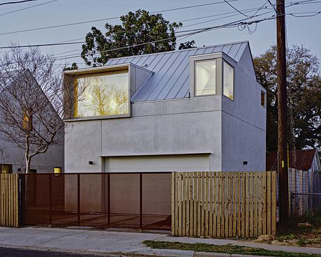 A modern, two-story residence with a striking angular roof, large windows, and a wooden fence.