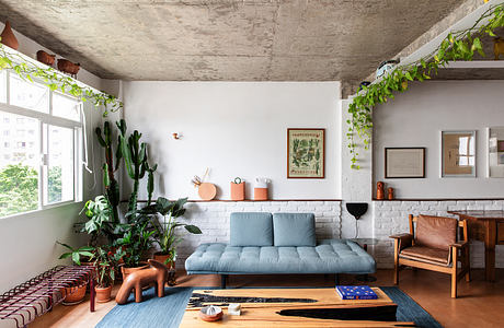 Cozy living room with cacti, potted plants, brick walls, and exposed concrete ceiling.