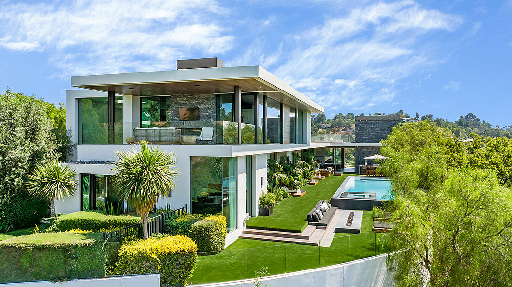 Modern glass and stone home surrounded by lush greenery and a swimming pool.