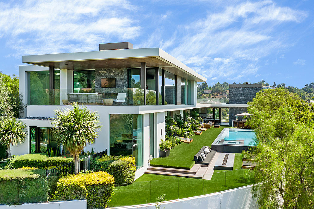 Modern glass and stone home surrounded by lush greenery and a swimming pool.