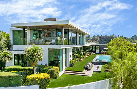 Modern glass and stone home surrounded by lush greenery and a swimming pool.