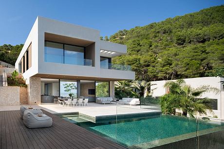 A modern, minimalist villa with a large glass facade, swimming pool, and lush greenery.