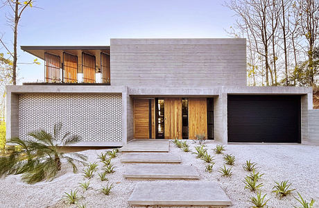 Modern concrete and wood residence with prominent entrance, garage, and balcony.