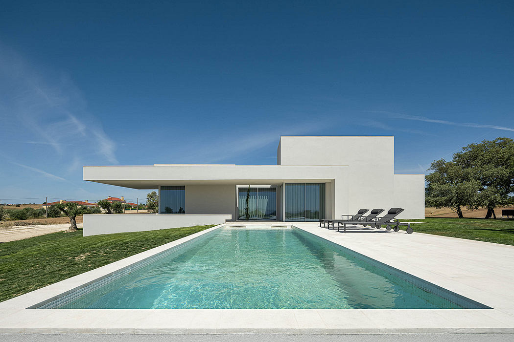 Modern white house with a large swimming pool and lounge chairs on a grassy lawn against a blue sky.
