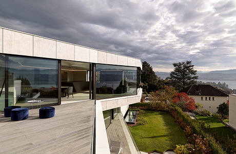 Modern, glass-walled house with a scenic lakeside view and well-landscaped garden.