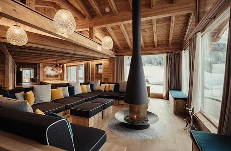 A cozy, rustic living room with a central fireplace and recessed lighting in a wooden cabin.