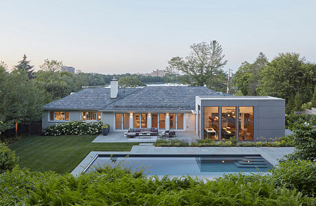 A modern home with expansive windows, a pool, and lush greenery surrounding it.