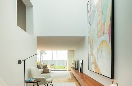 A modern and minimalist living room with a large abstract artwork, wooden furniture, and a view to the exterior.