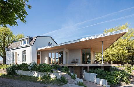 Modern architecture with a unique slanted roof, large windows, and a patio overlooking lush greenery.