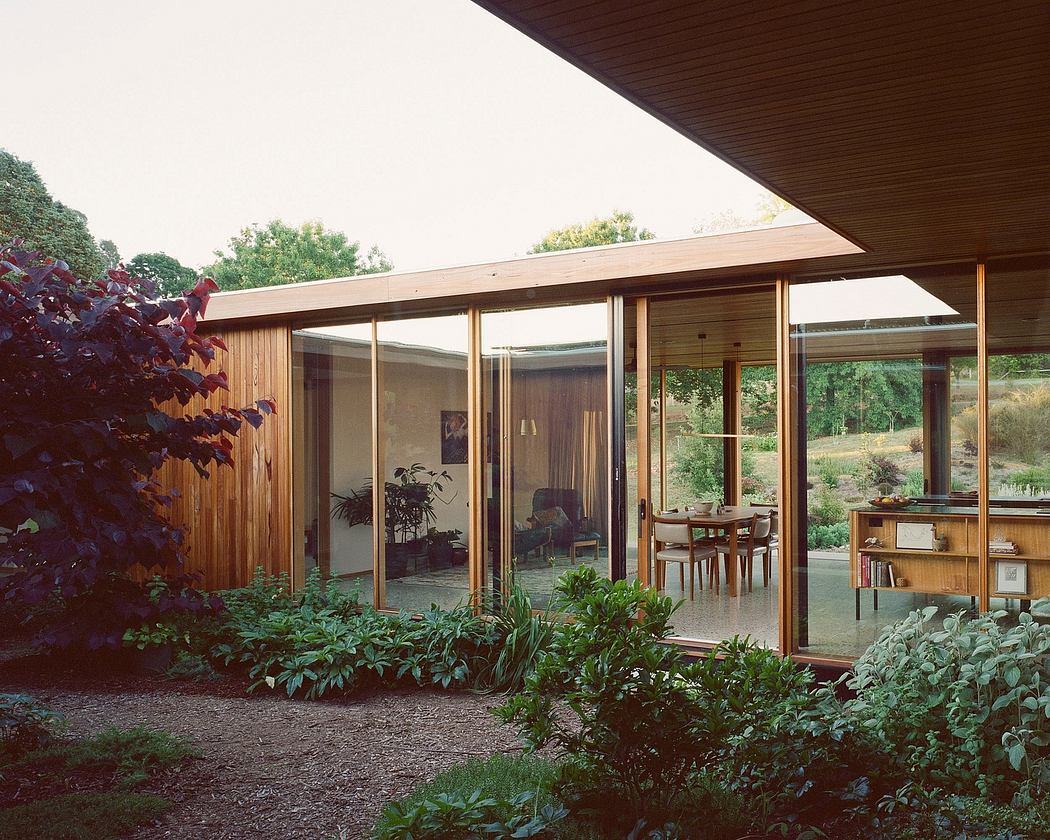 A mid-century modern home with floor-to-ceiling glass walls, a wooden exterior, and lush vegetation.
