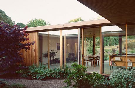 A mid-century modern home with floor-to-ceiling glass walls, a wooden exterior, and lush vegetation.