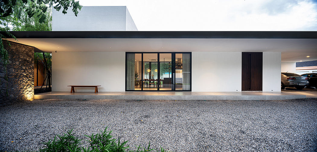 A modern, minimalist home with large windows, a covered patio, and a gravel-covered driveway.