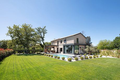 Stylish modern house with glass walls, lush lawn, and well-manicured landscape.