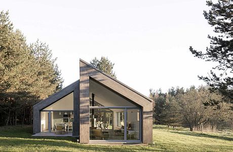 Modern, minimalist cabin with glass walls and gable roof nestled in a forested setting.