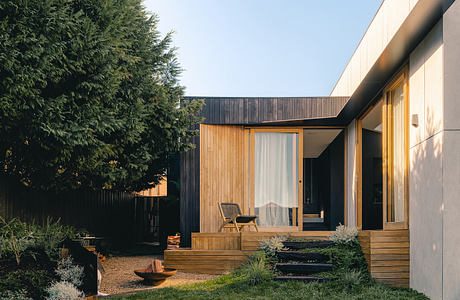 Modern cabin-style home with wooden siding, covered porch, and lush landscaping.